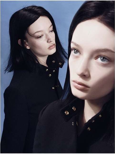 Two women with short black hair in black buttoned jackets, photographed indoors against a light blue backdrop.