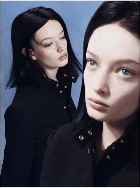 Two women with short black hair in black buttoned jackets, photographed indoors against a light blue backdrop.