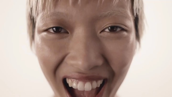 Extreme close-up of an adult female's face with a bright smile, showcasing white teeth and bleached hair against a plain background.