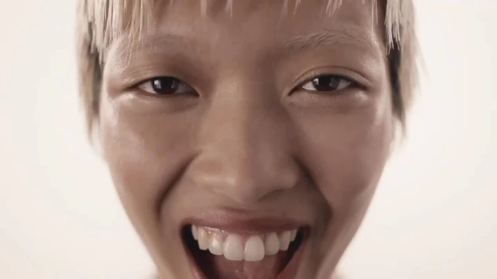 Extreme close-up of an adult female's face with a bright smile, showcasing white teeth and bleached hair against a plain background.