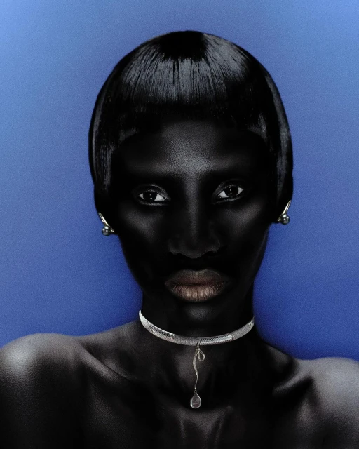 Close-up studio portrait of a dark-skinned woman with a short, shiny black hairstyle, wearing a silver choker against a blue background.