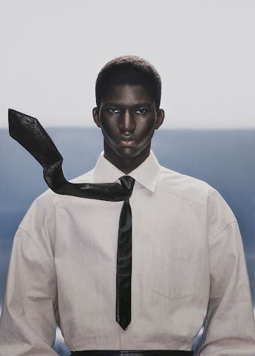 Black man wearing a white collared shirt with a black tie blowing in the wind against a pale horizon