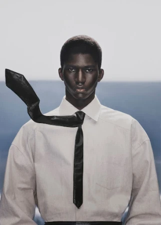 Black man wearing a white collared shirt with a black tie blowing in the wind against a pale horizon