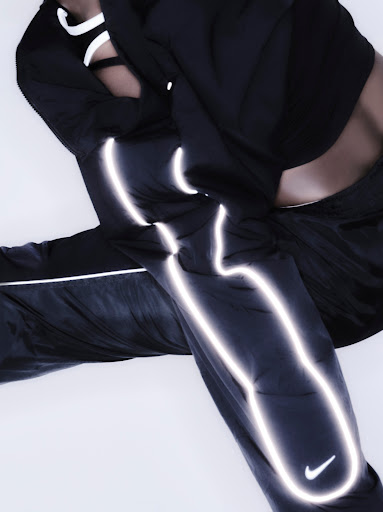 An athletic person poses in black nylon pants and a matching top. Silver reflective accents and a Nike logo add to the sporty aesthetic.