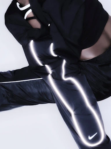 An athletic person poses in black nylon pants and a matching top. Silver reflective accents and a Nike logo add to the sporty aesthetic.