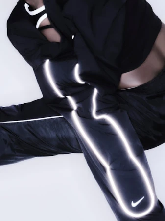An athletic person poses in black nylon pants and a matching top. Silver reflective accents and a Nike logo add to the sporty aesthetic.