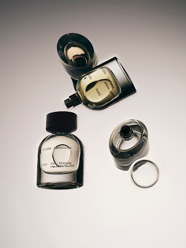 Still life shot of perfume bottles with black caps and clear glass casing, some with lids off, on an off-white gradient background.