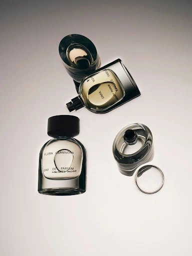 Still life shot of perfume bottles with black caps and clear glass casing, some with lids off, on an off-white gradient background.