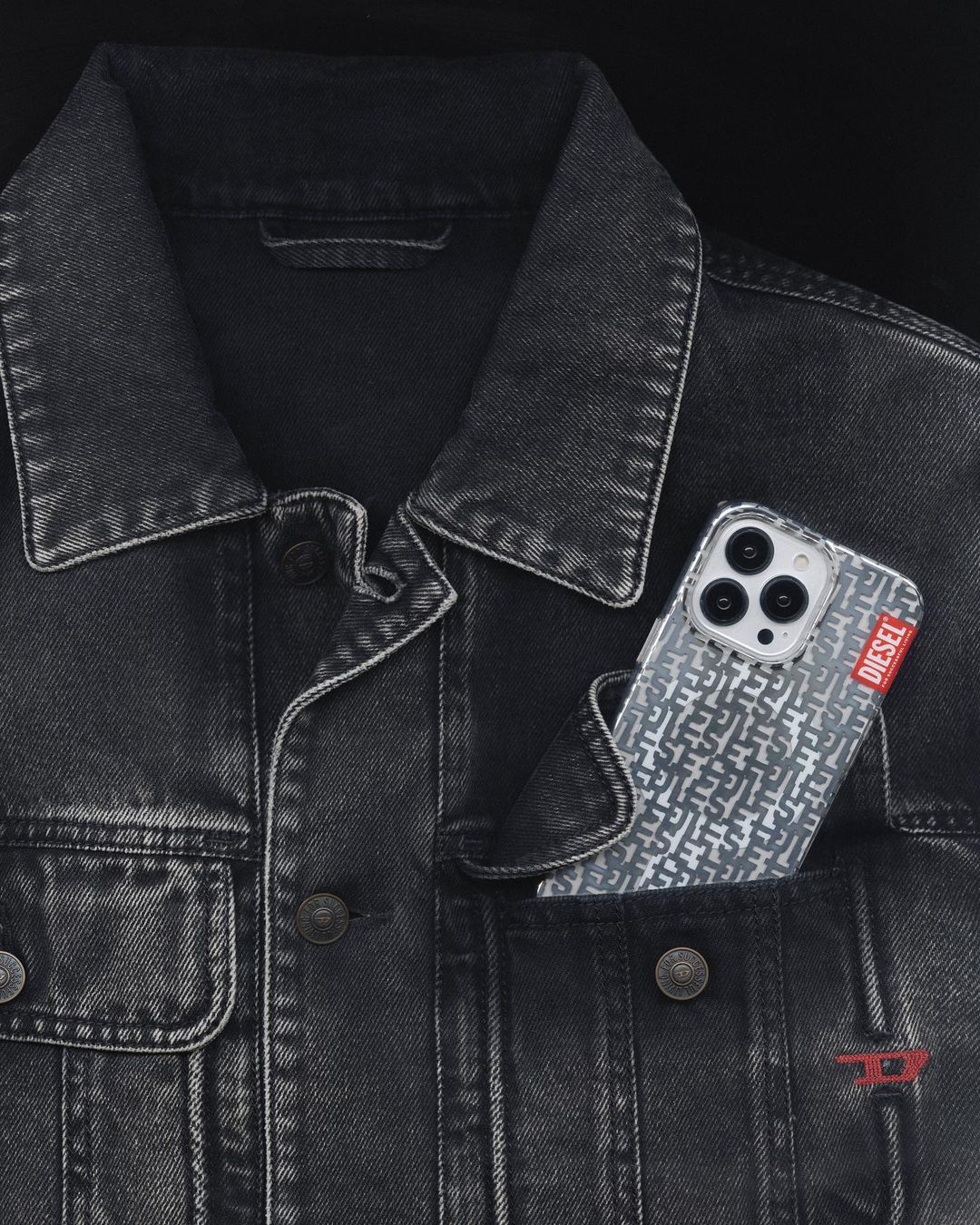 Close-up of a black denim jacket with a Diesel-branded phone case in the pocket, featuring a pattern of interlocking 'D' logos.