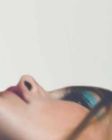 Close-up side profile of a woman with vibrant blue eyeshadow and dark hair, set against a plain light background.
