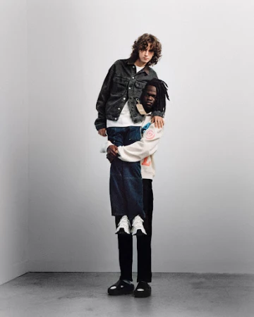 Two men in a minimalist photo studio. One man is giving the other a piggyback ride, both are wearing fashionable casual outfits.