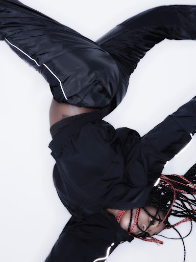 An athletic young woman in a black tracksuit does a handstand against a white backdrop, showcasing fitness and strength with style.