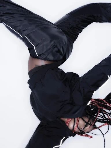 An athletic young woman in a black tracksuit does a handstand against a white backdrop, showcasing fitness and strength with style.