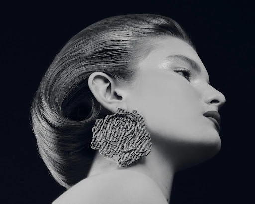 Black and white portrait of a woman in profile, wearing a large denim flower earring, with a sleek updo hairstyle against a dark backdrop.