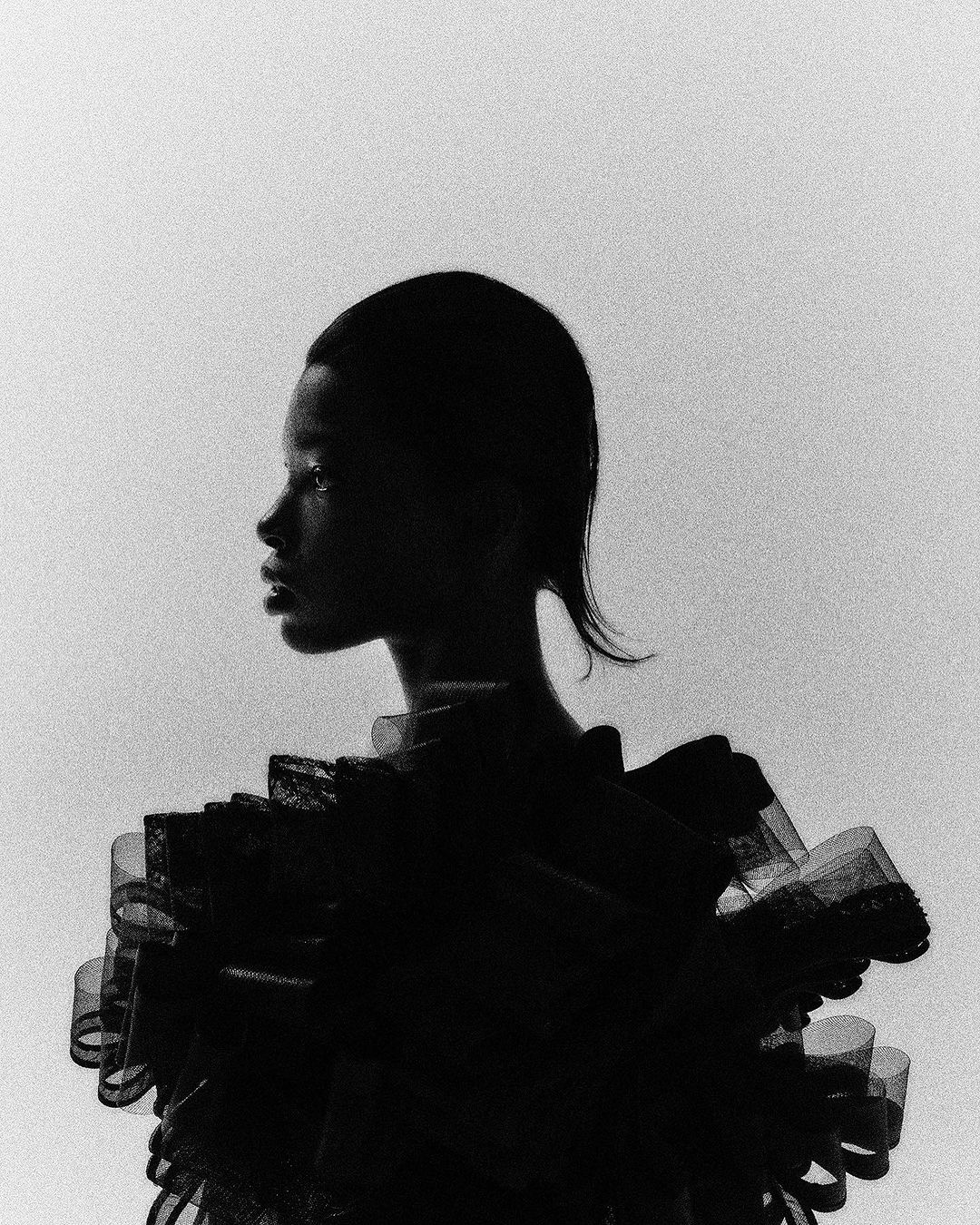 Monochrome fashion portrait of an adult woman in a distinctive ruffled collar, captured in a studio setting with soft, diffused lighting.