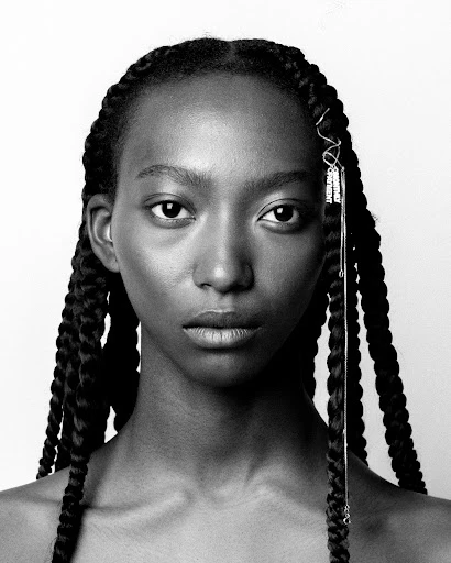 Close-up black and white portrait of a young woman with braided hair, adorned with silver hair accessories, against a white background.