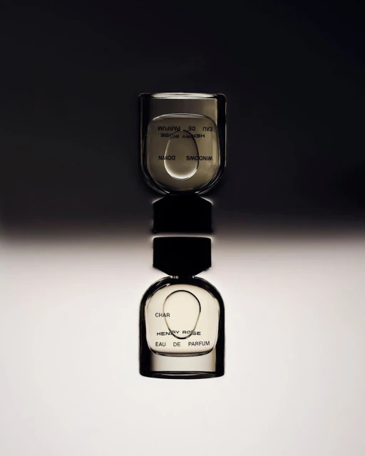 Two Henry Rose Eau de Parfum bottles, stacked vertically, on a reflective surface with a dark background and soft, indirect lighting.