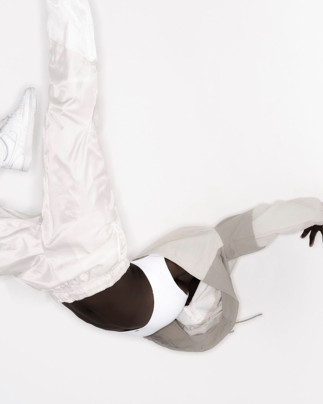 Studio shot of a person wearing a white and gray tracksuit with black and white sports bra and white sneakers on a white background.