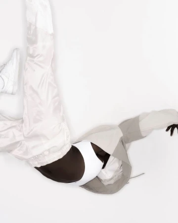 Studio shot of a person wearing a white and gray tracksuit with black and white sports bra and white sneakers on a white background.