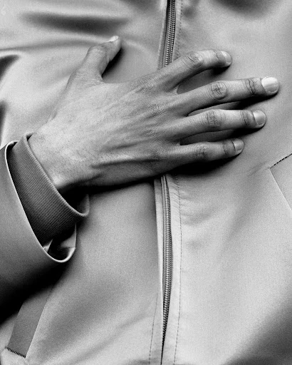 Monochrome close-up of an adult's hand with fingers splayed resting on a jacket with a visible zipper.