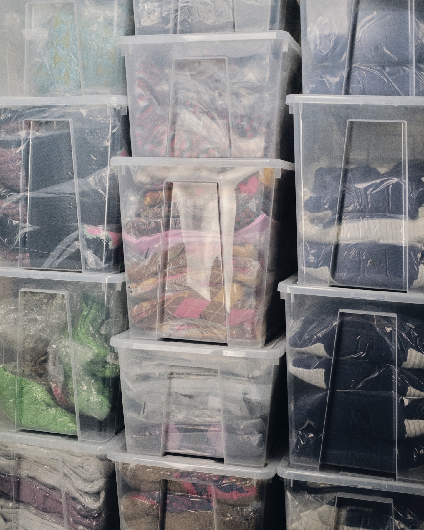 Stack of clear plastic storage containers filled with various items; containers are stacked vertically, filling the frame.
