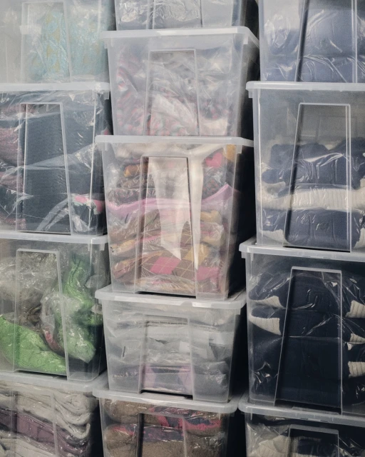 Stack of clear plastic storage containers filled with various items; containers are stacked vertically, filling the frame.