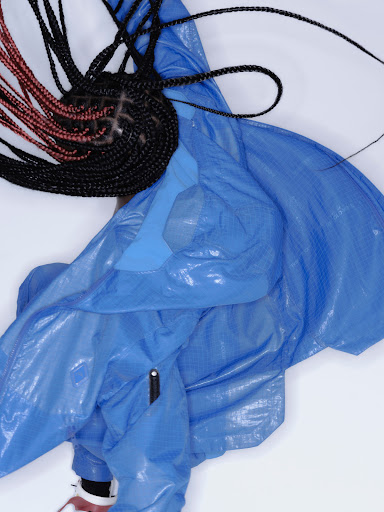 Model in vibrant blue jacket with black and red braided hair against a plain white background captured overhead