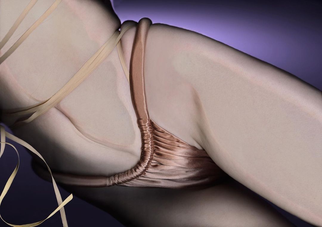 Woman's body featuring a gold-colored string top against a purple background in a studio shot highlighting curves and skin texture.
