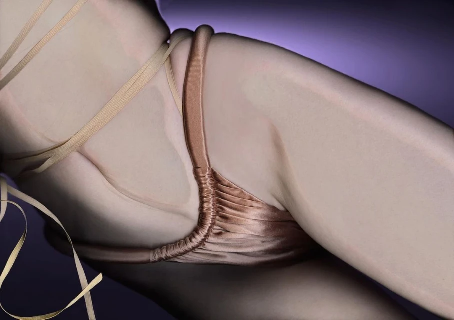 Woman's body featuring a gold-colored string top against a purple background in a studio shot highlighting curves and skin texture.