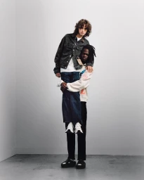 Two male models posing against a white studio wall, one being held in a piggyback lift by the other.