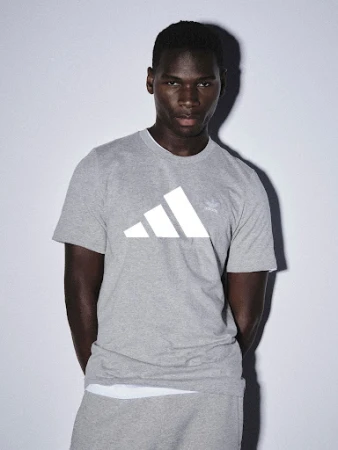 Black man wearing a grey Adidas t-shirt and matching sweatpants standing against a plain grey seamless background.