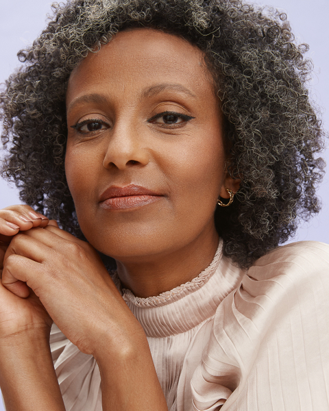 Close-up of a Black woman with graying curly hair, fair complexion, wearing a beige silk top with her hands gently placed under her chin.