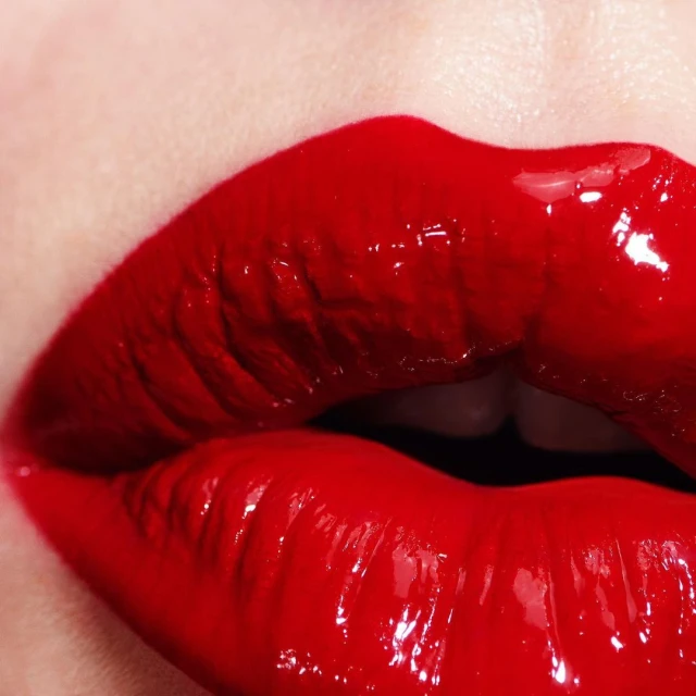 Close-up shot of a woman's face featuring glossy red lips with a full pout and visible white teeth, conveying bold beauty.