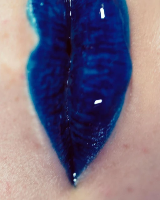 Close-up studio shot of a person's skin with a thick streak of vibrant blue liquid running down, creating a striking visual contrast.