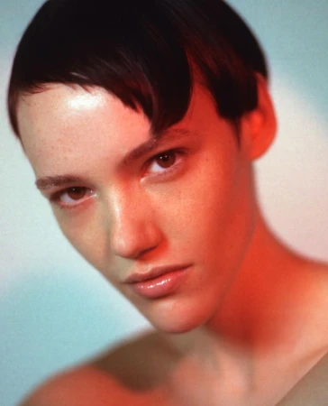 Close-up portrait of a woman with short dark hair and freckles illuminated by warm red light by photographer Anairam