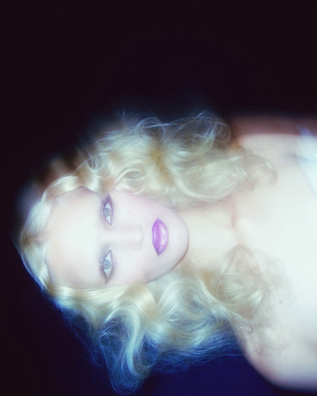 Portrait of a blonde woman with soft focus and motion blur, wearing vivid purple lipstick against a dark background