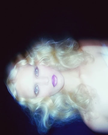 Portrait of a blonde woman with soft focus and motion blur, wearing vivid purple lipstick against a dark background