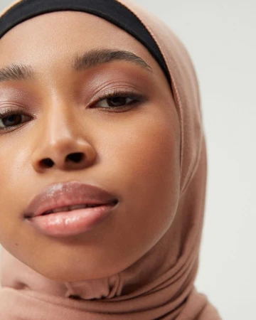 Close-up portrait of a black woman wearing a beige hijab and black headband against a light background.