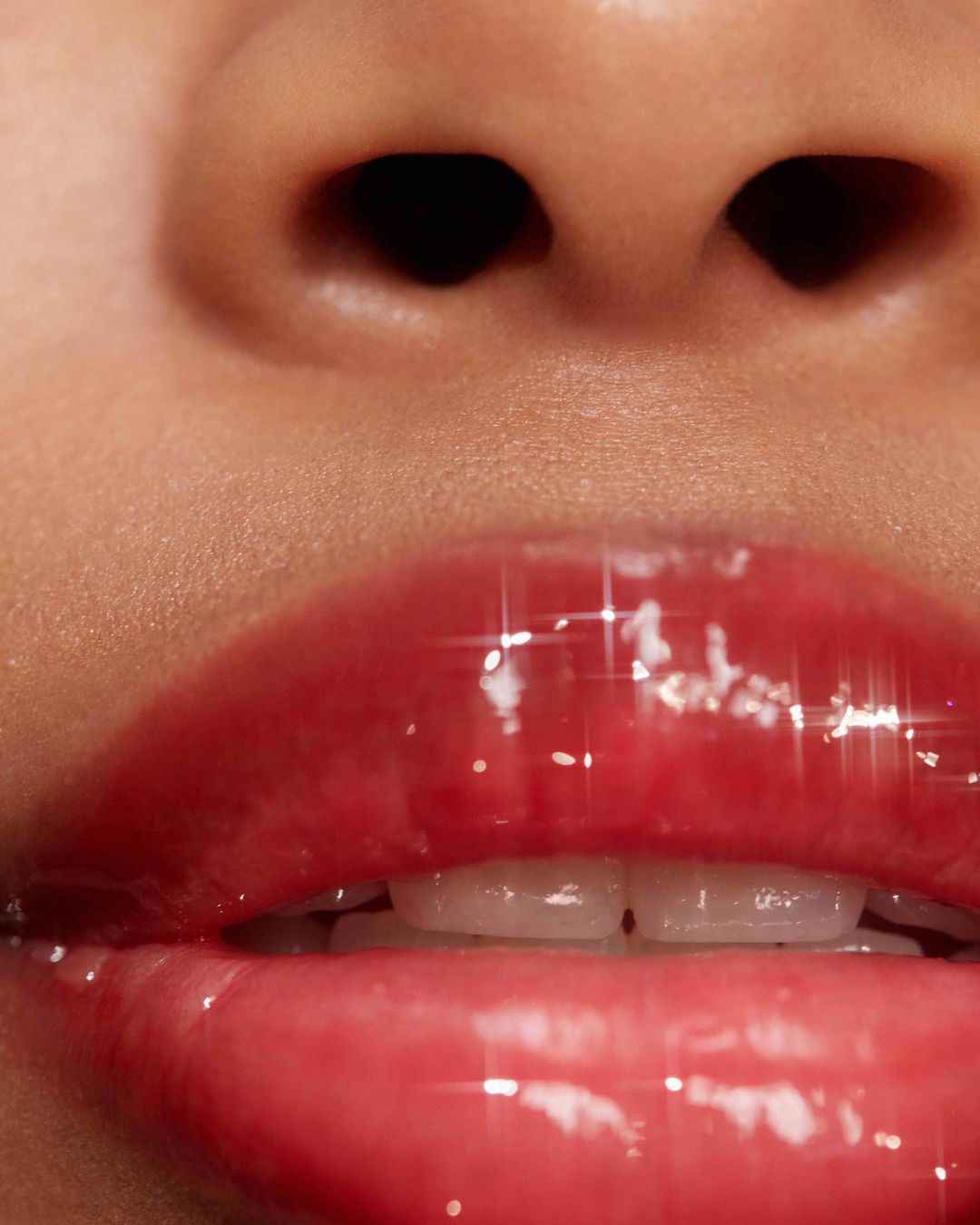 Close-up of adult female's face with glossy pink lips, visible teeth, and nose. The skin has a smooth texture and a soft glow.