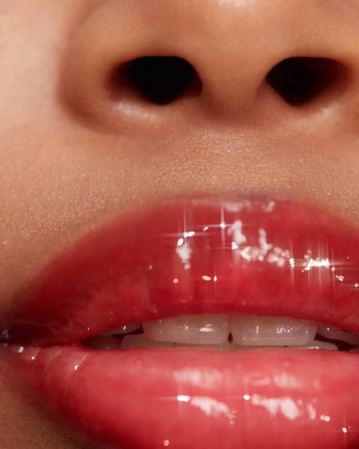 Close-up of adult female's face with glossy pink lips, visible teeth, and nose. The skin has a smooth texture and a soft glow.
