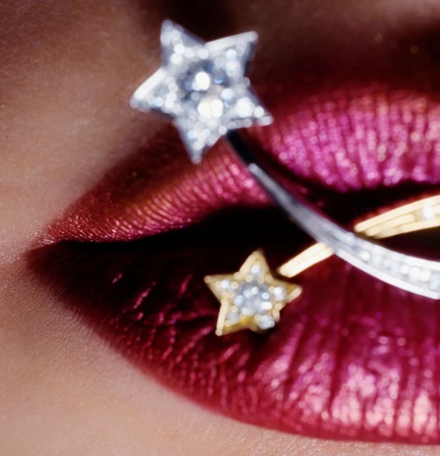Close-up of a woman's red lips adorned with two gold and silver star-shaped jewellery pieces, creating a sparkling and fashionable effect.