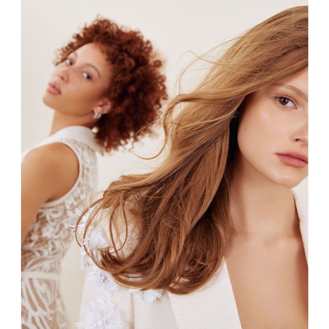 Close-up of two women in a photo studio. The woman in the foreground has wavy light brown hair and the woman in the back has auburn curly hair.