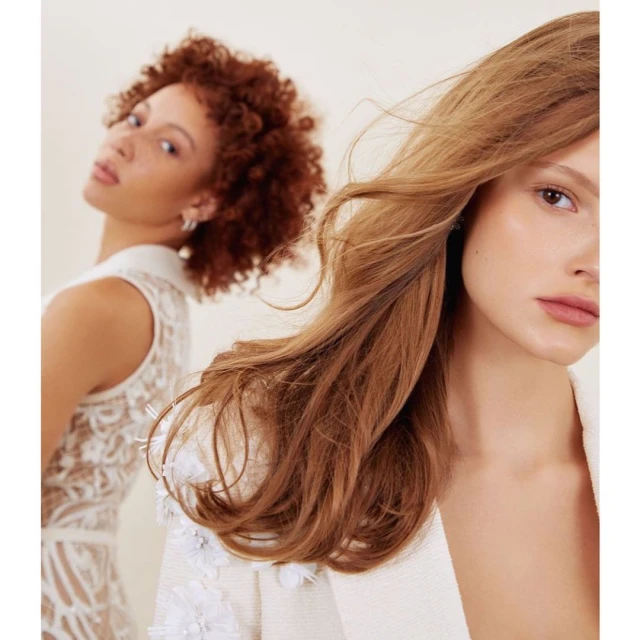 Close-up of two women in a photo studio. The woman in the foreground has wavy light brown hair and the woman in the back has auburn curly hair.