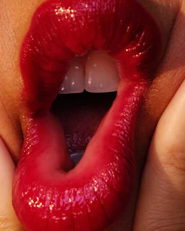 Close-up of parted lips with glossy red lipstick revealing upper teeth, photographed by Anairam.
