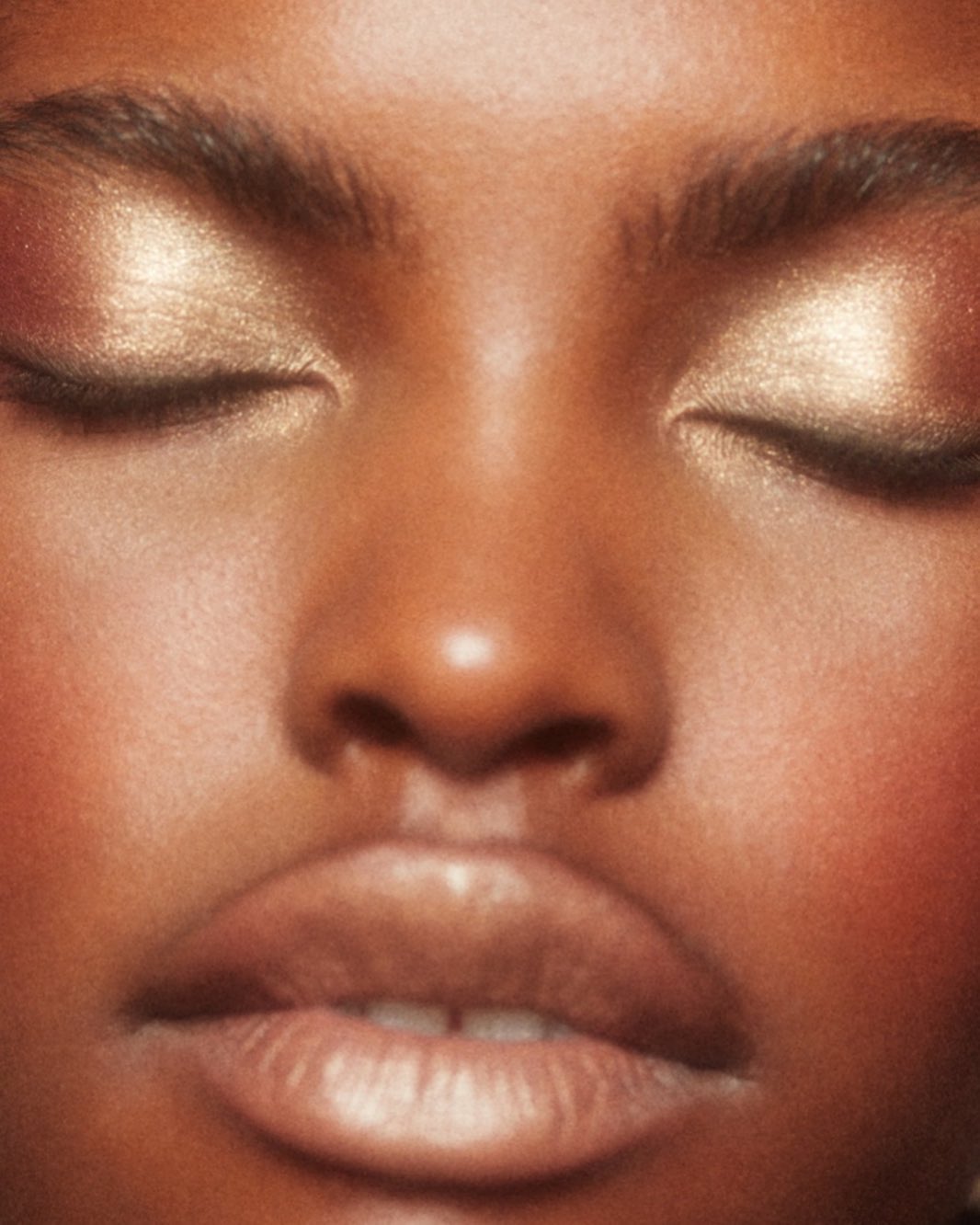 Close-up portrait of a Black woman with shimmering gold eyeshadow and glowing skin by photographer Anairam.