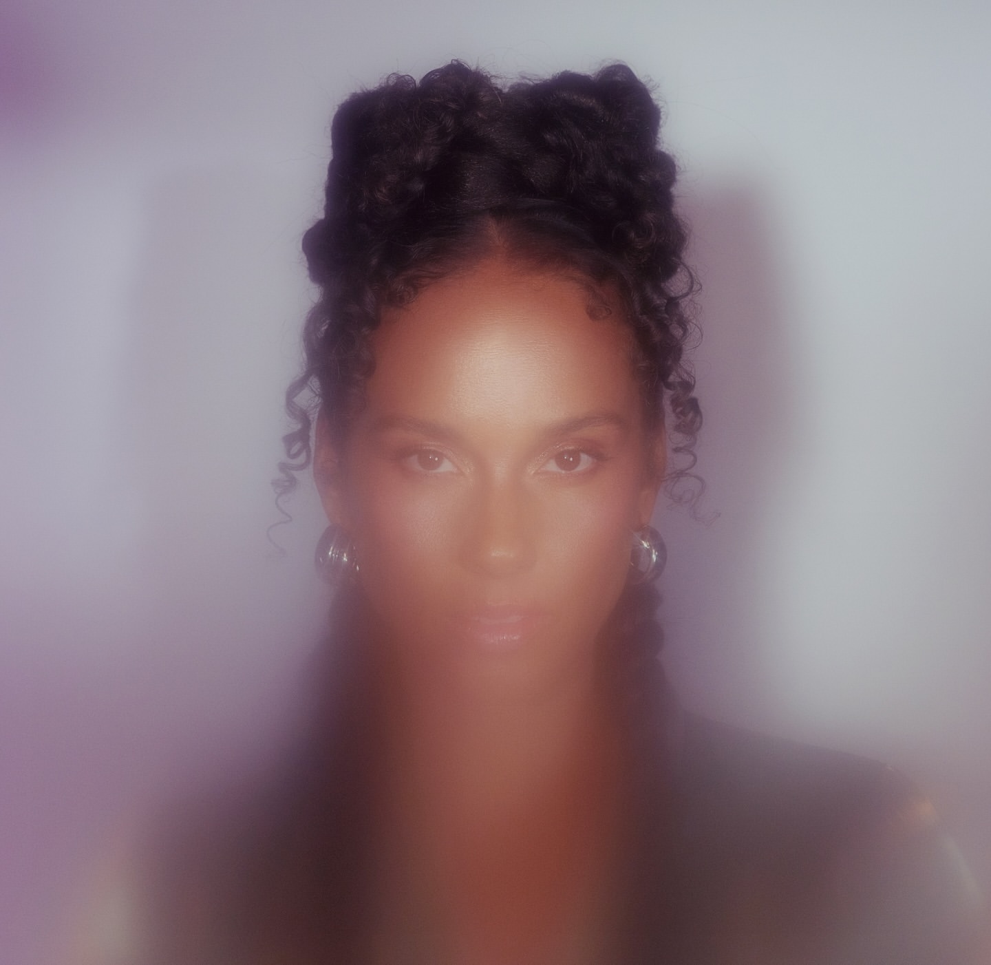 Portrait of a woman with braided updo hairstyle and silver hoop earrings against a soft glowing white background