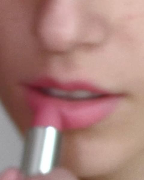 Close-up of a person applying pink lipstick with a silver tube, focusing on the lower face and lips.