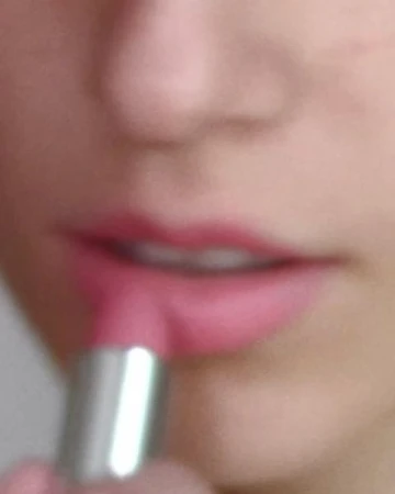 Close-up of a person applying pink lipstick with a silver tube, focusing on the lower face and lips.
