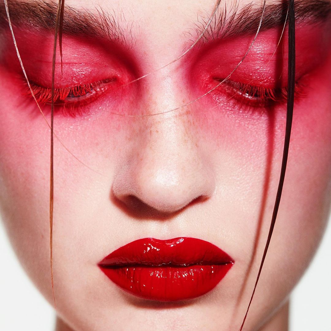 Close-up of a young woman's face with red eyeshadow and glossy red lips, highlighting beauty makeup, and artistic makeup style.