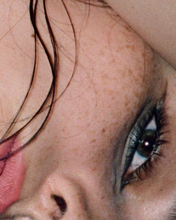 Extreme close-up portrait of a woman showing dark eye makeup, freckles, and dark hair strands by Anairam